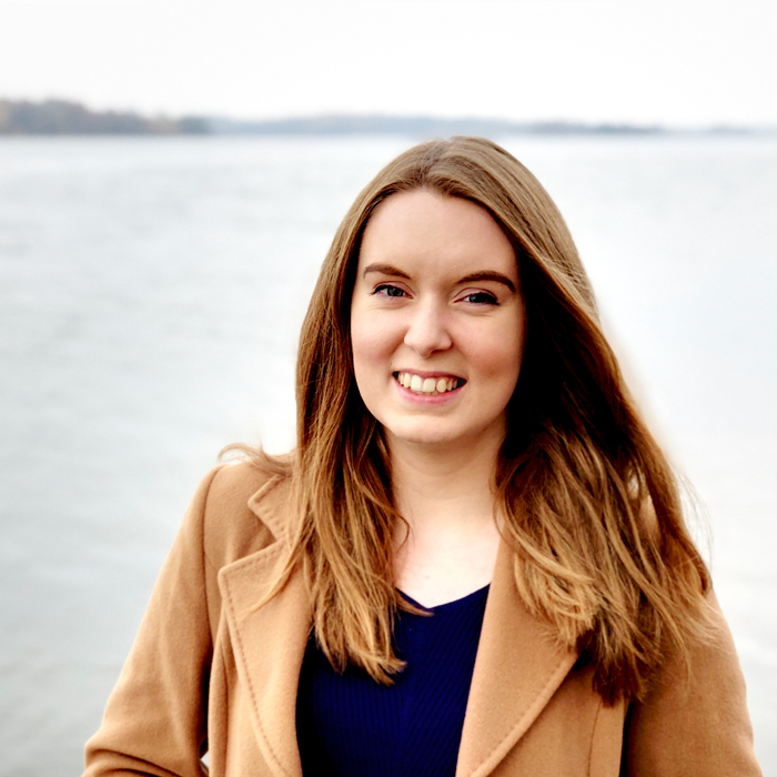 Jenny Brennan - a brown-haired woman stood infront of the sea